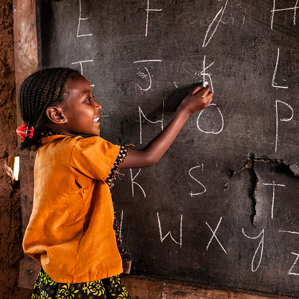 istockphoto-599779728-612×612 African little girl during english class class in very remote school. The bricks that make up the walls of the school are made of clay and straw. There is no light and electricity inside the classroom